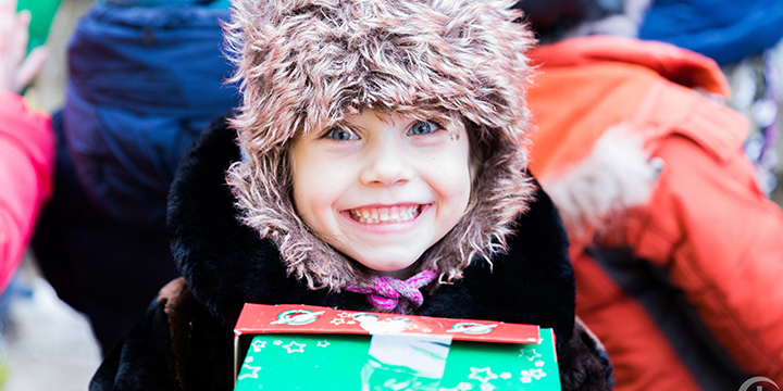 Girl in fluffy hat smiles with shoebox
