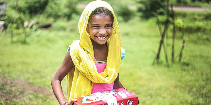Girl in yellow holding shoebox smiling