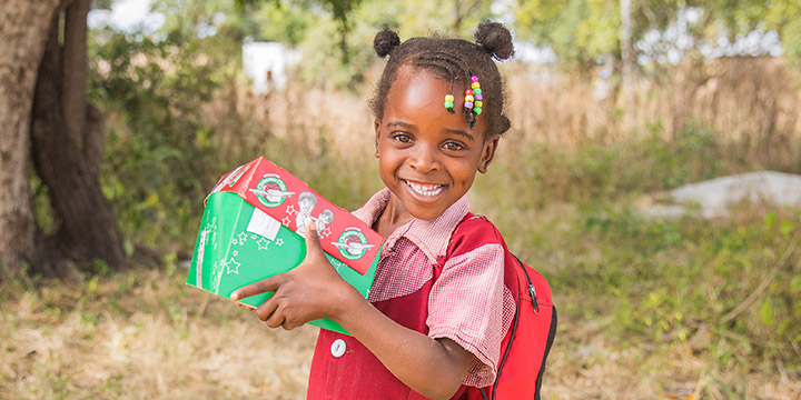 Girl in red dress smiles holding shoebox gift