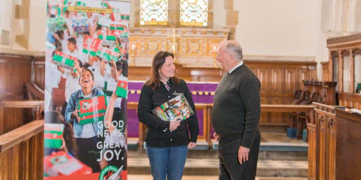 Project leader and vicar by Operation Christmas Child banner