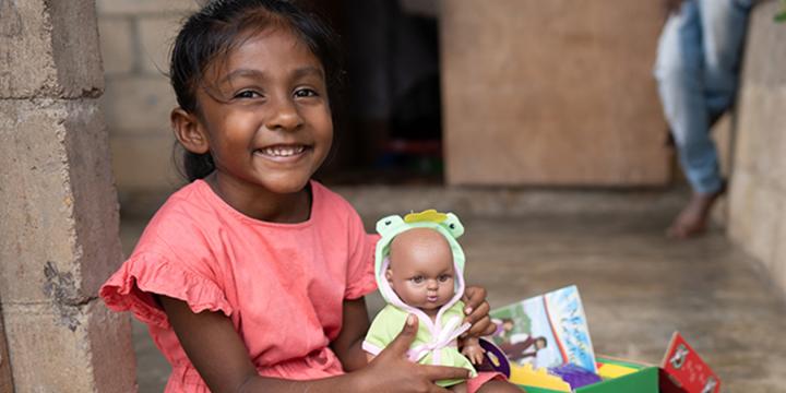 Girl in pink dress smiling holding new doll