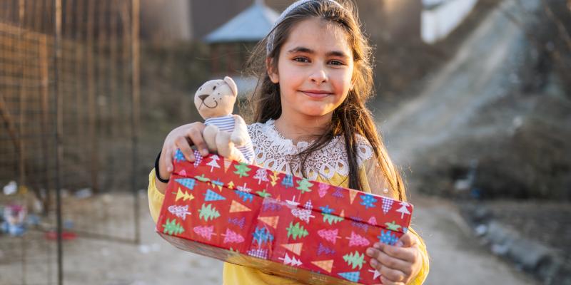 girl in yellow jumper holding red shoebox and teddy