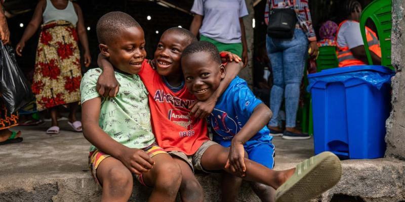 Three friends laugh on the church steps while their parents wait for care inside. In a place marked by hardship, childhood joy remains resilient.