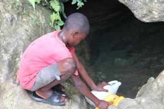 A Haitian boy draws water with household containers. The search for water can lead to whatever spring or river is available.