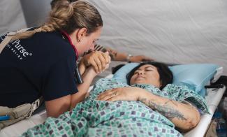 In the Emergency Field Hospital, nurse Jamie prays with a patient named Sanda who lost her husband in the earthquake.