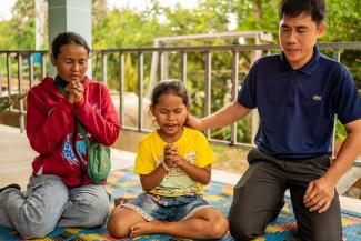 Tola (centre) joins Pastor Kosal (right) in prayer at a community event.